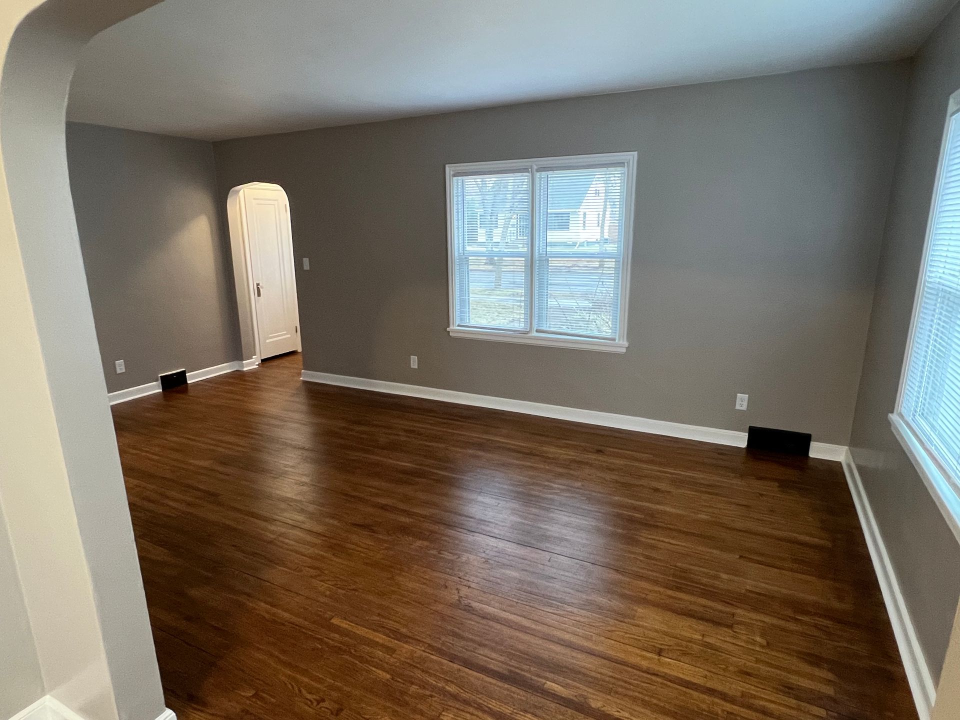 An empty living room with hardwood floors and two windows.