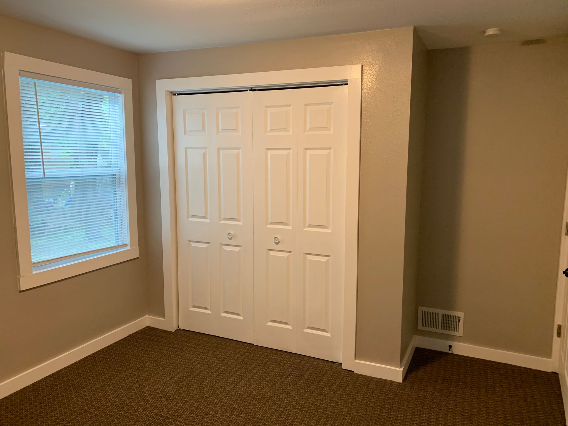 An empty room with a closet and a window.