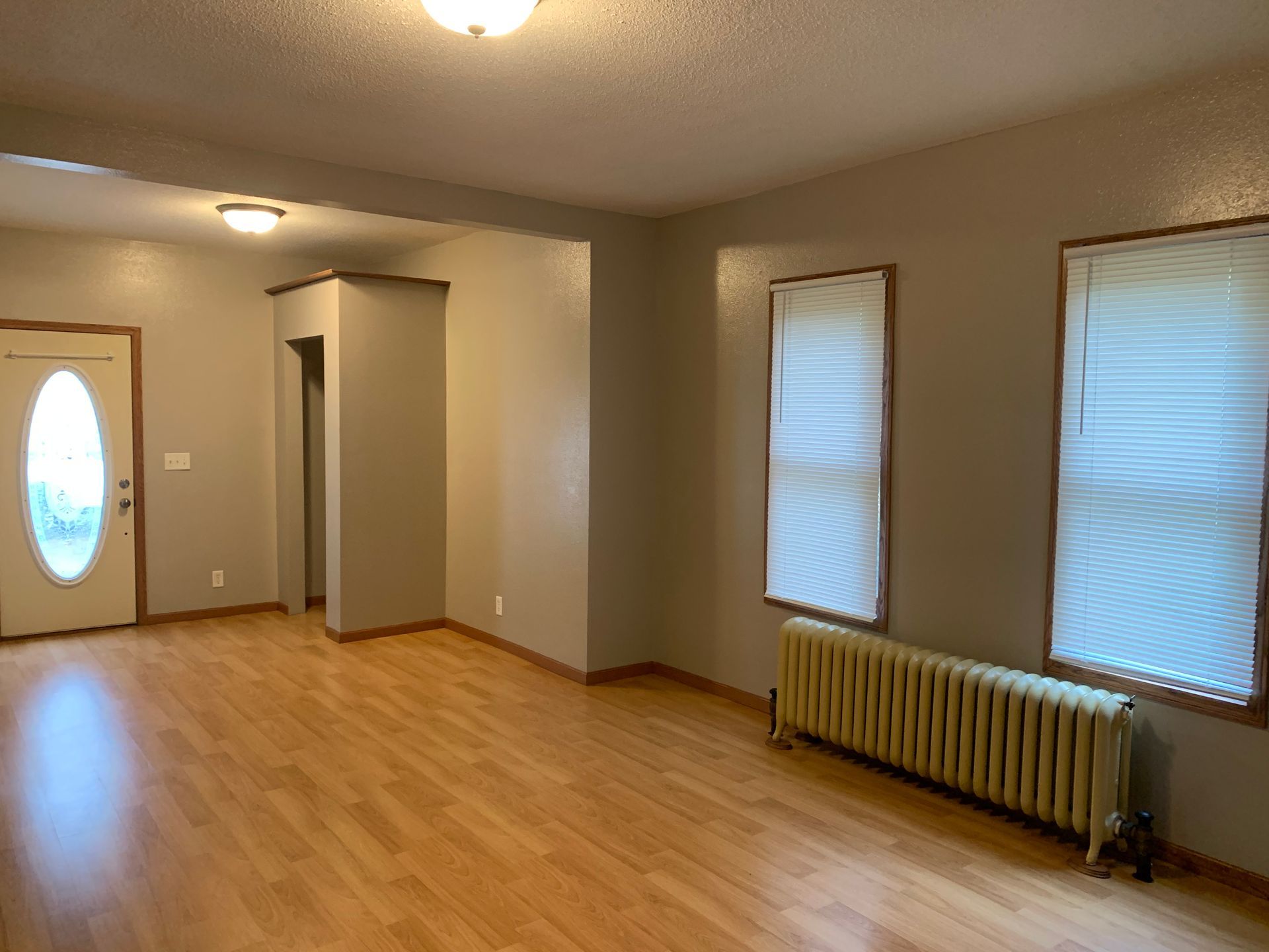 An empty living room with hardwood floors and a radiator.