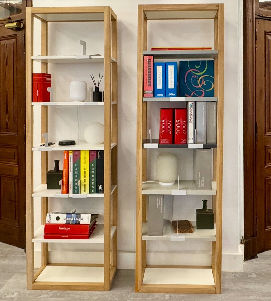 Dos estanterías de madera con libros, carpetas y utensilios de cocina contra una pared.