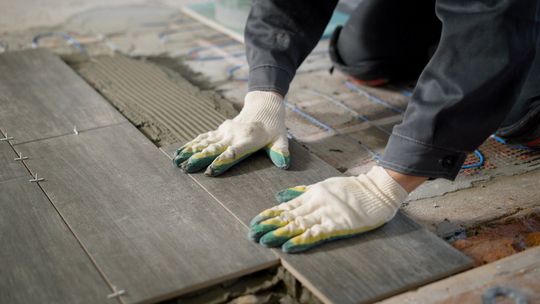 A person wearing gloves is laying tiles on the floor.