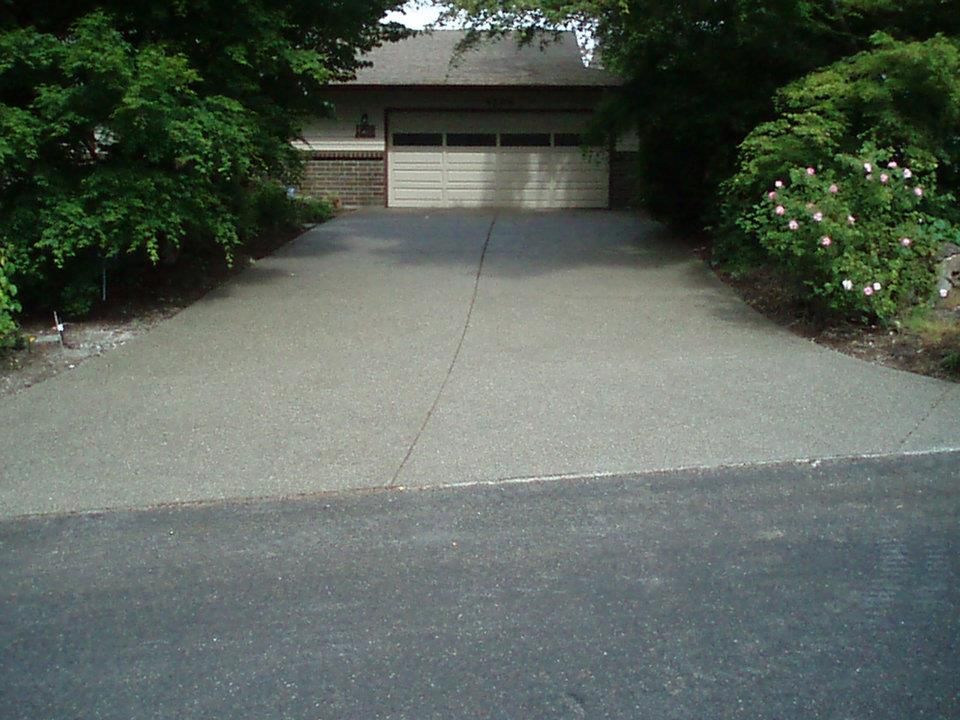 Exposed aggregate concrete driveway bordered by dense landscaping