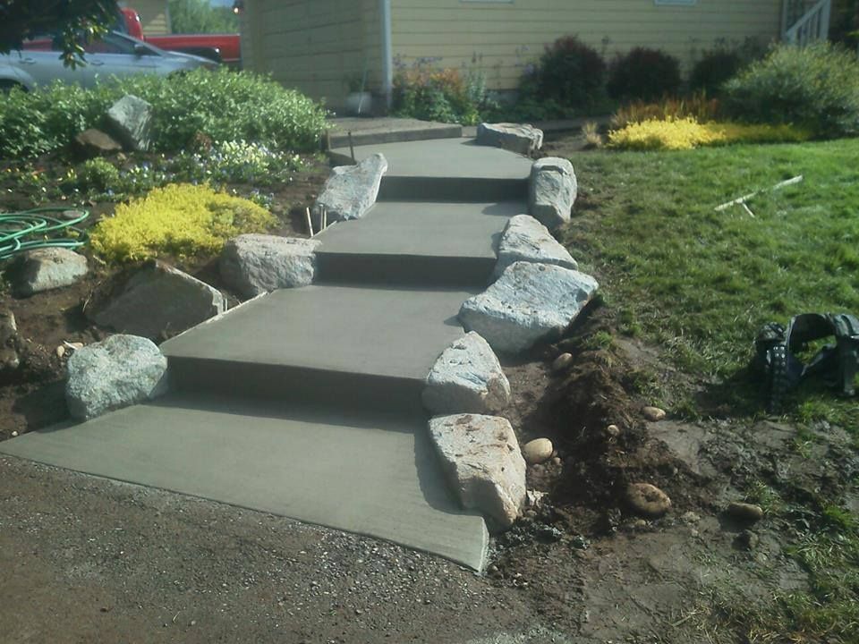 Custom concrete landscape steps with natural boulder borders leading up sloped front yard