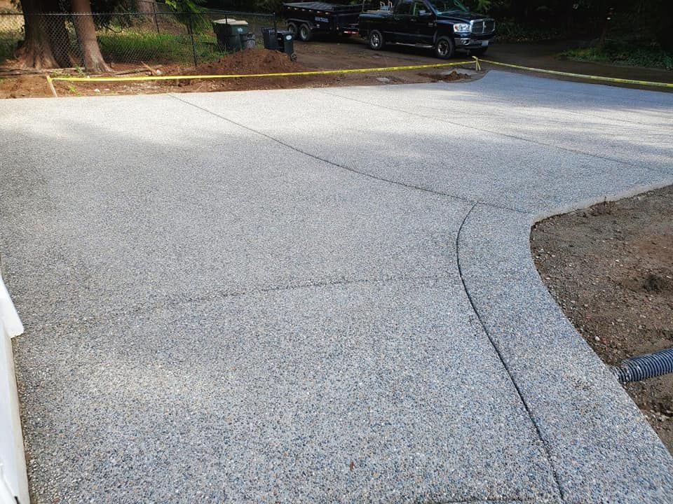 Newly installed exposed aggregate concrete driveway with flowing curved border
