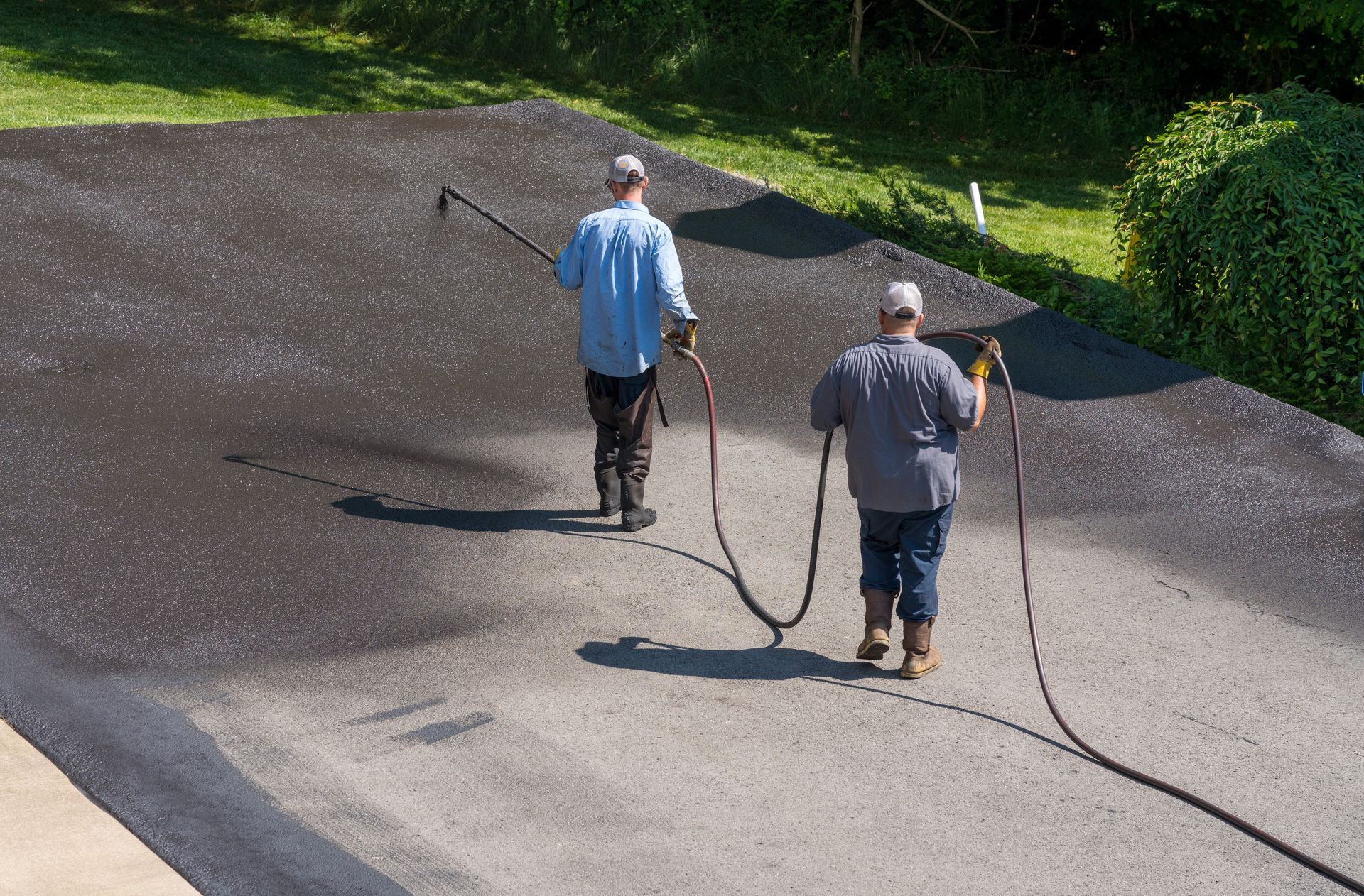 Workers applying blacktop sealer to asphalt street using a spray to provide a protective coat against the elements.