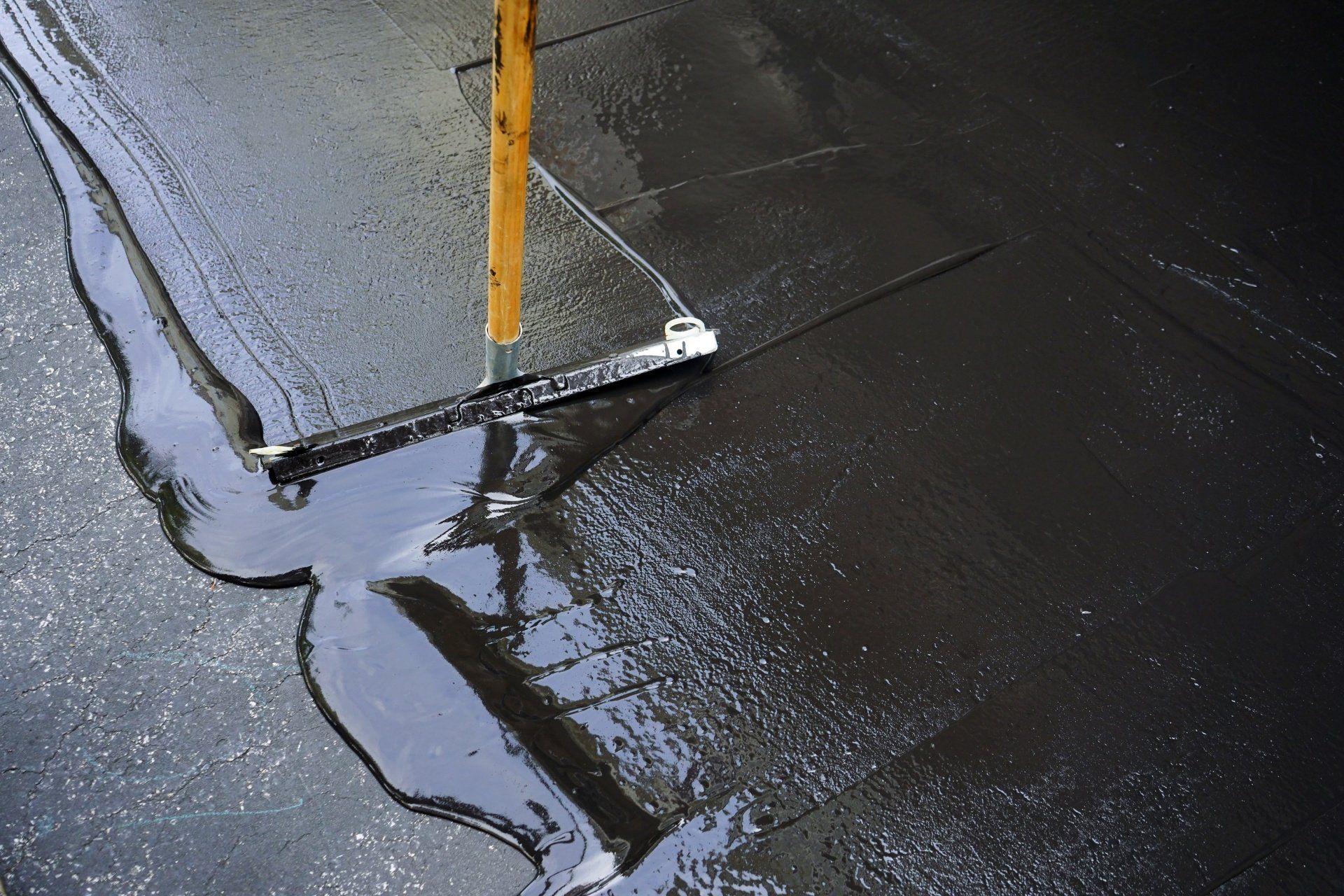 A person applies a layer of sealcoating to an asphalt driveway, ensuring its protection and longevity.