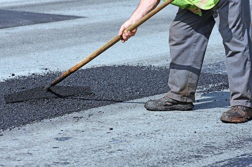 Image of workers repairing a damaged asphalt road, using tools to fill cracks and smooth the surface, ensuring safe and smooth transportation.