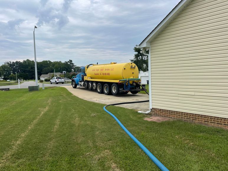 A yellow truck is parked in front of a house with a blue hose attached to it.