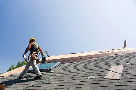 A man is standing on top of a roof holding a piece of wood.