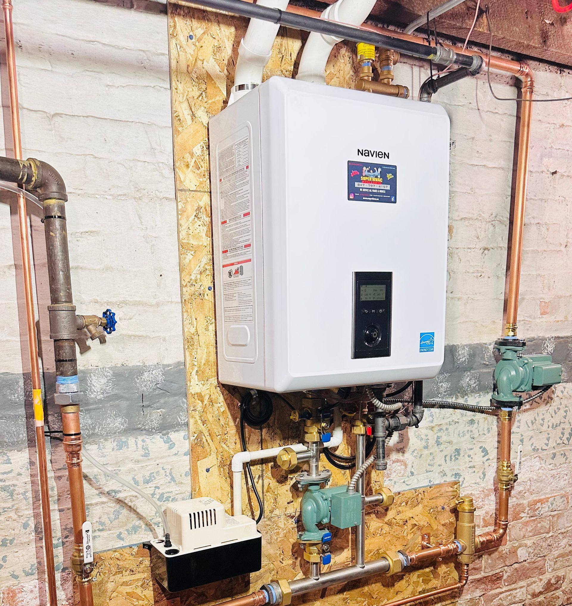 White tankless water heater on a wooden panel against a concrete wall, with copper pipes and valves.