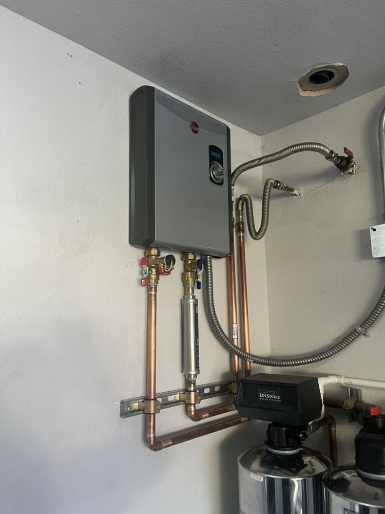 Tankless water heater installed on a wall with copper pipes and a water softener.