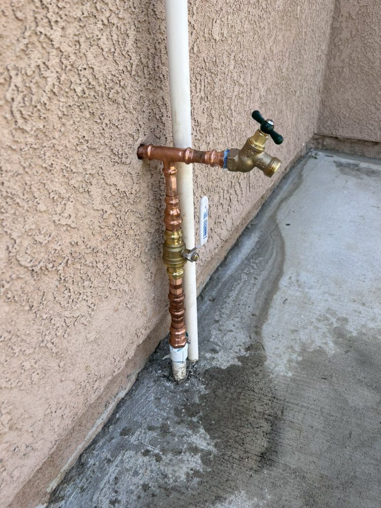 Copper pipes and spigot connected to a wall, with a white pipe and concrete floor.