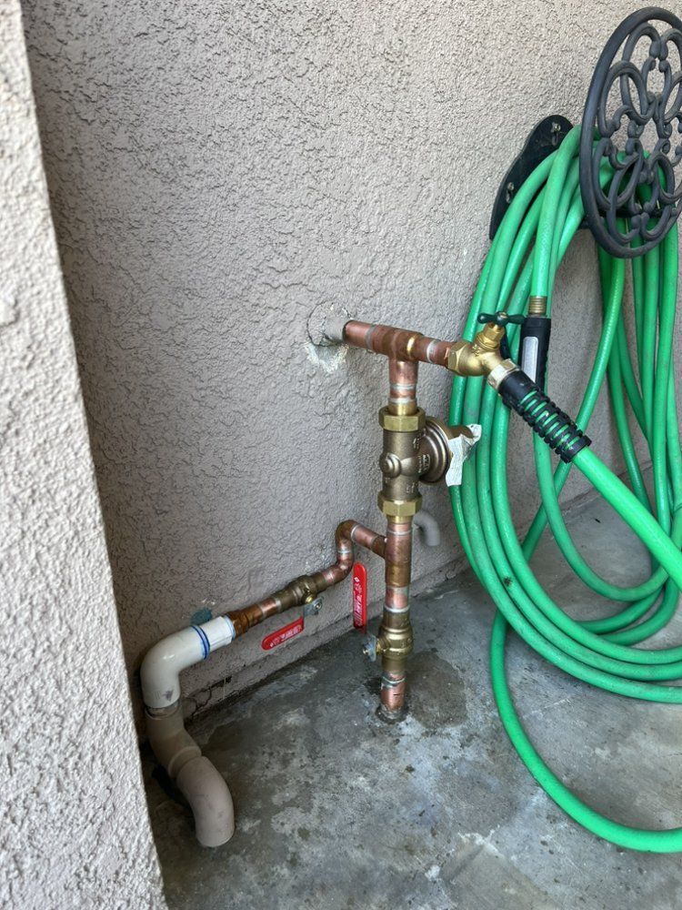 Copper water pipes and hose connected to an outdoor faucet on a stucco wall.
