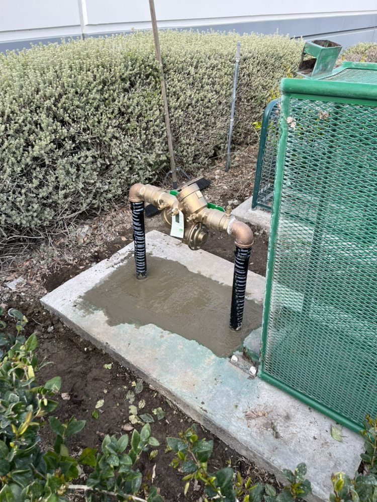 A concrete box with water pipes and a valve, with a green wire mesh enclosure next to it.