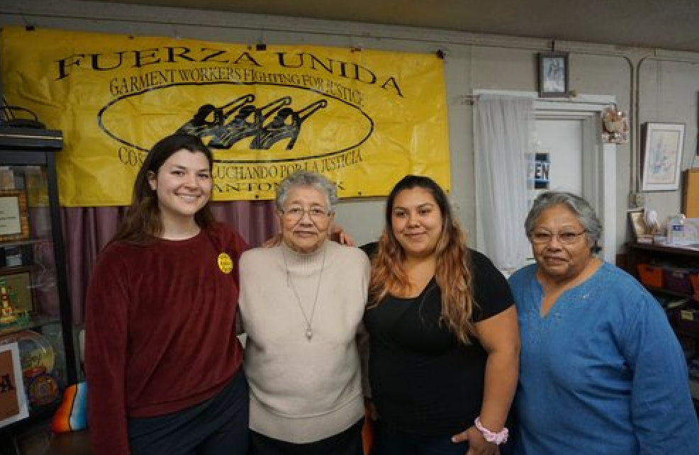 A group of women are posing for a picture in front of a yellow banner.