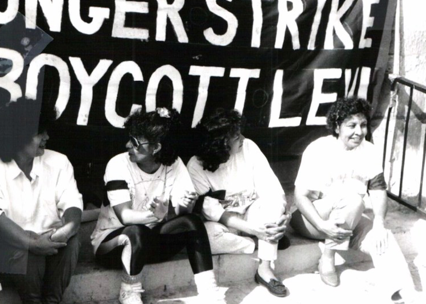 A group of people sit in front of a sign that says boycott lew