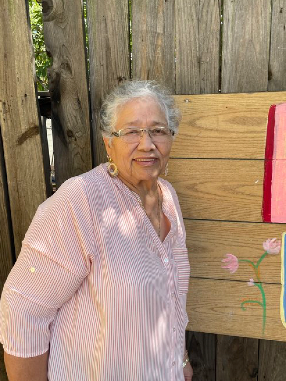 A woman in a pink shirt is standing in front of a wooden fence.