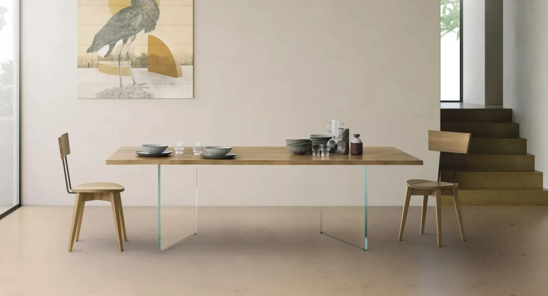 Sala da pranzo minimalista con tavolo in legno, due sedie, quadri alle pareti e scale sulla destra.