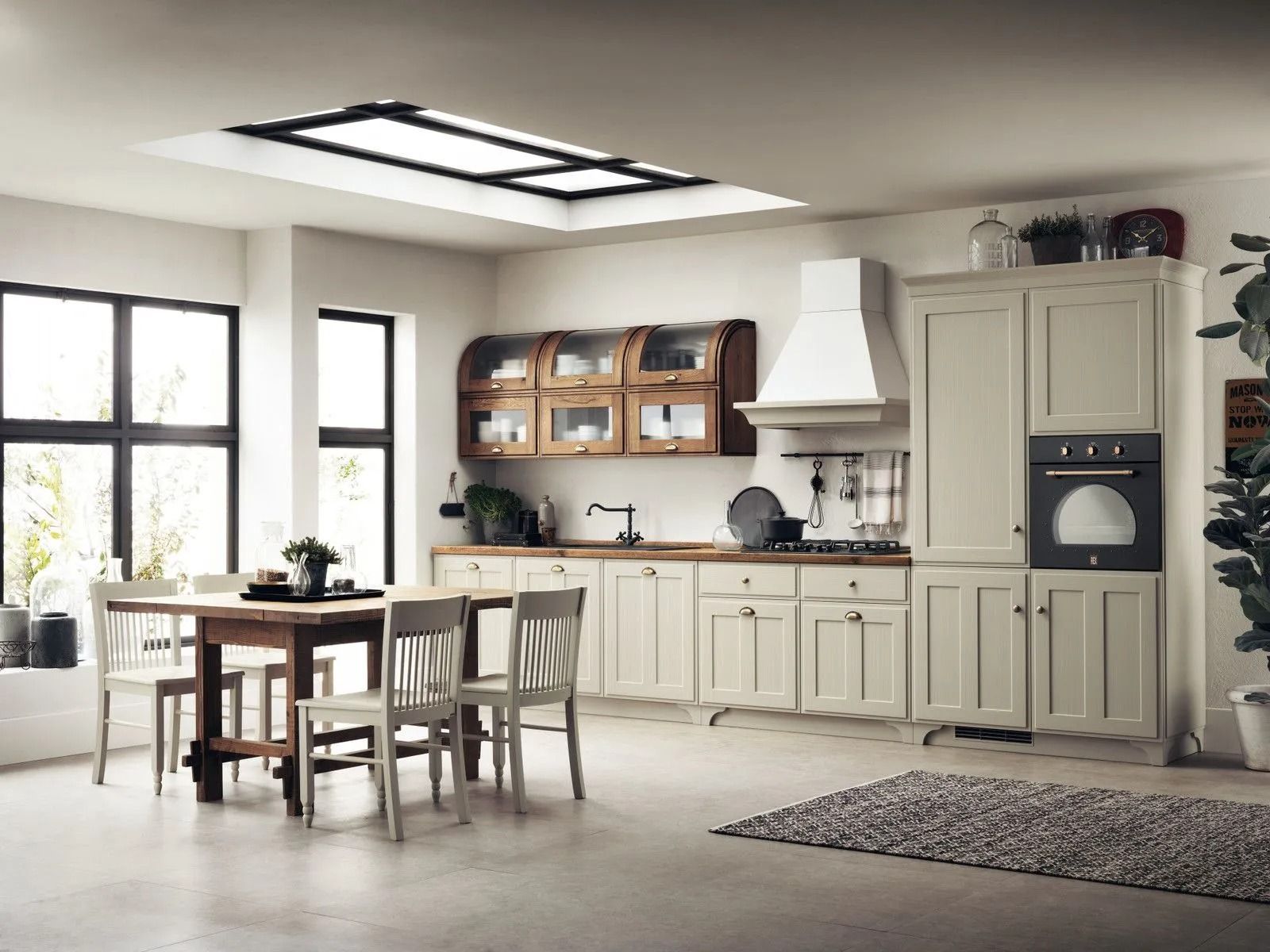 Cucina moderna e luminosa con tavolo da pranzo, mobili color crema e ampie finestre, delicatamente illuminate da lucernari.