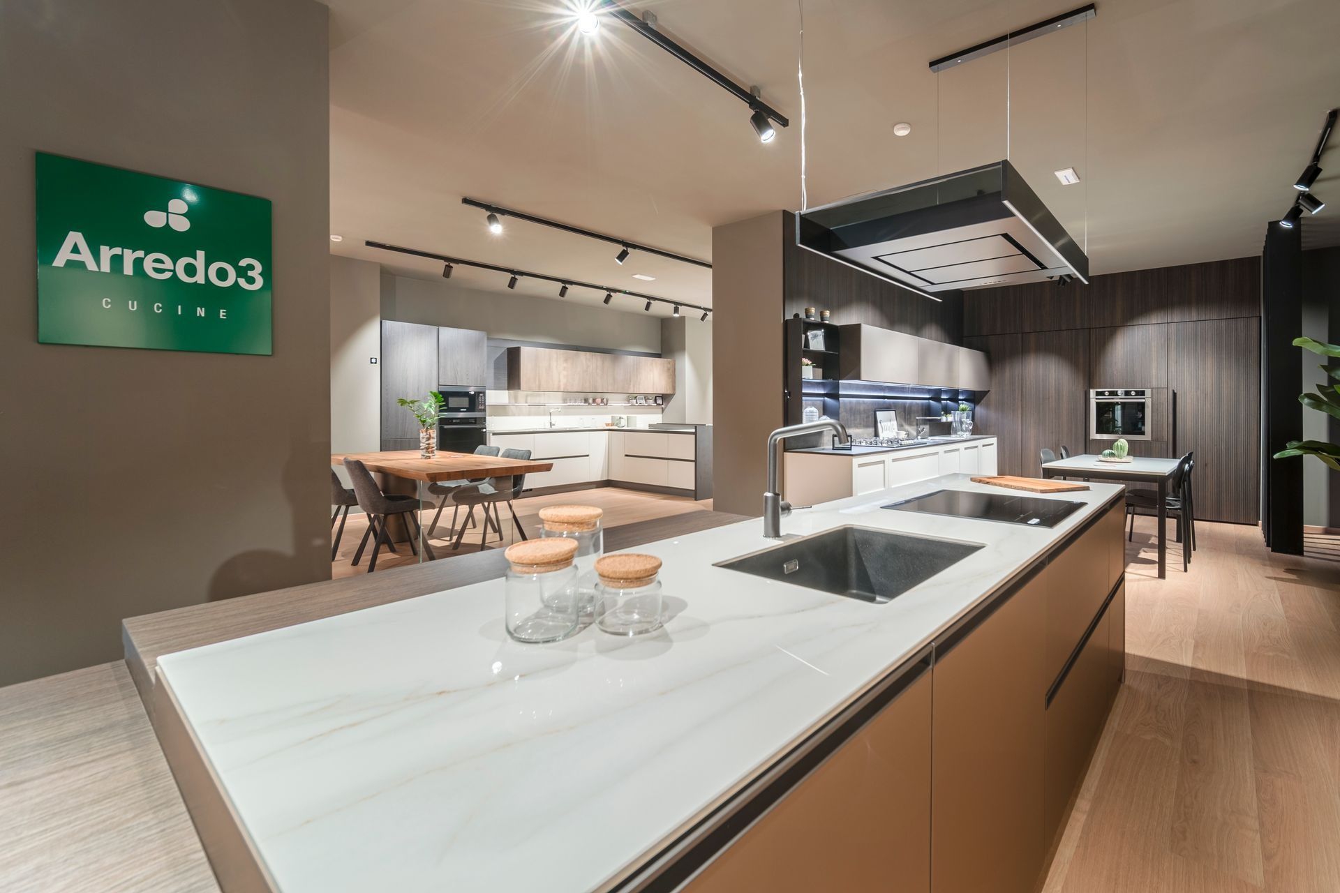 Cucina moderna con mobili in legno scuro, isola marrone e tavolo da pranzo in un luminoso interno minimalista.