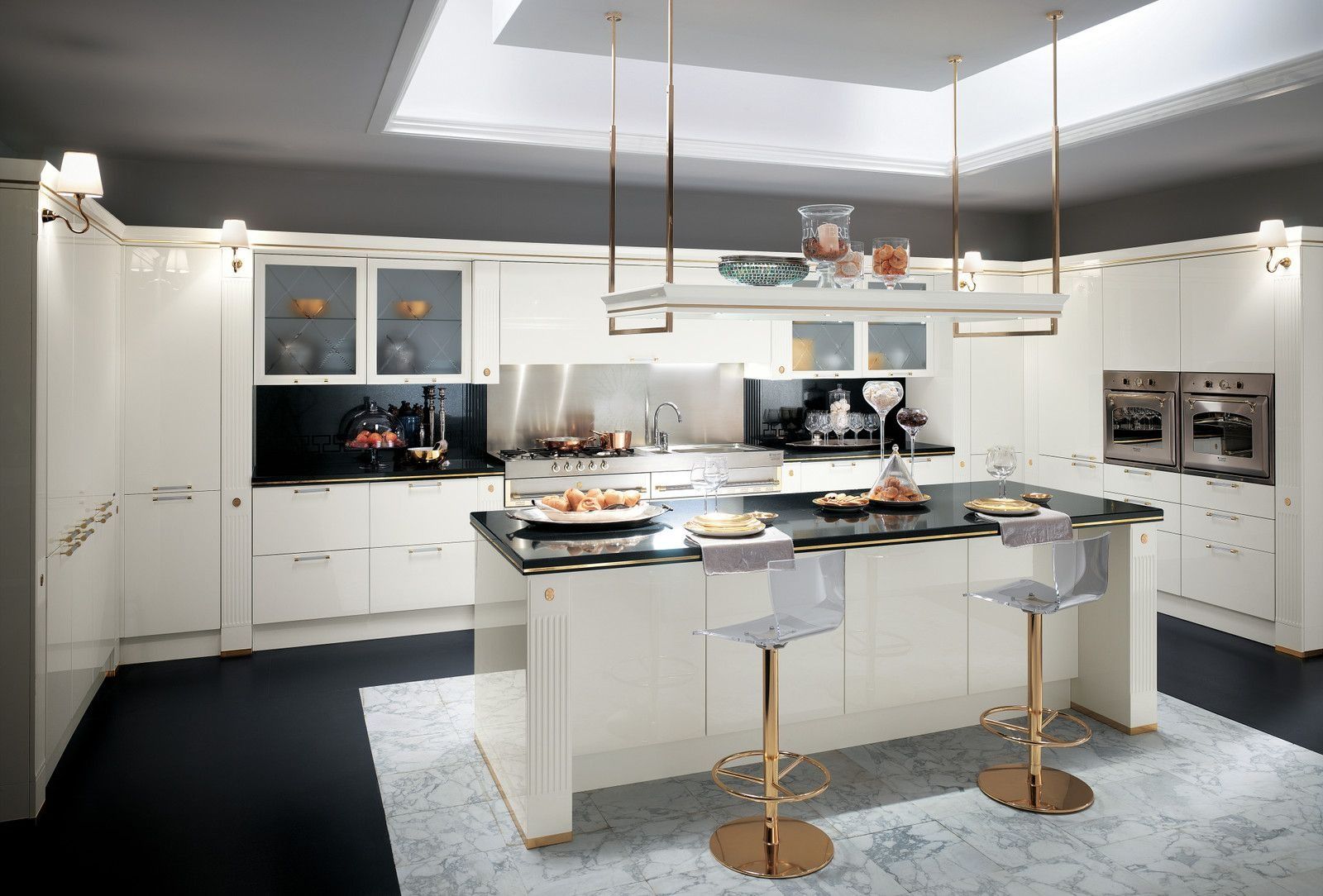 Cucina moderna bianca con isola, sgabelli da bar, lampade a sospensione e forni a incasso.