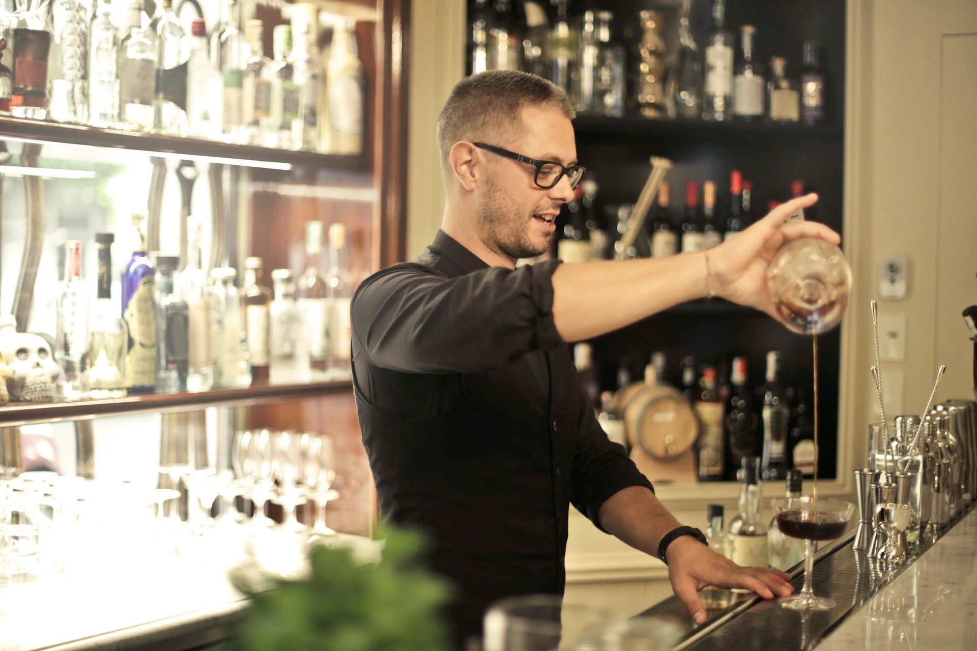 A man behind a counter is pouring cocktail drinks.