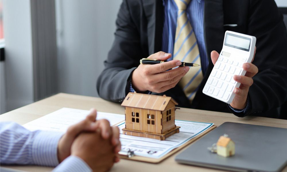 broker holding a phone, with miniature house on table