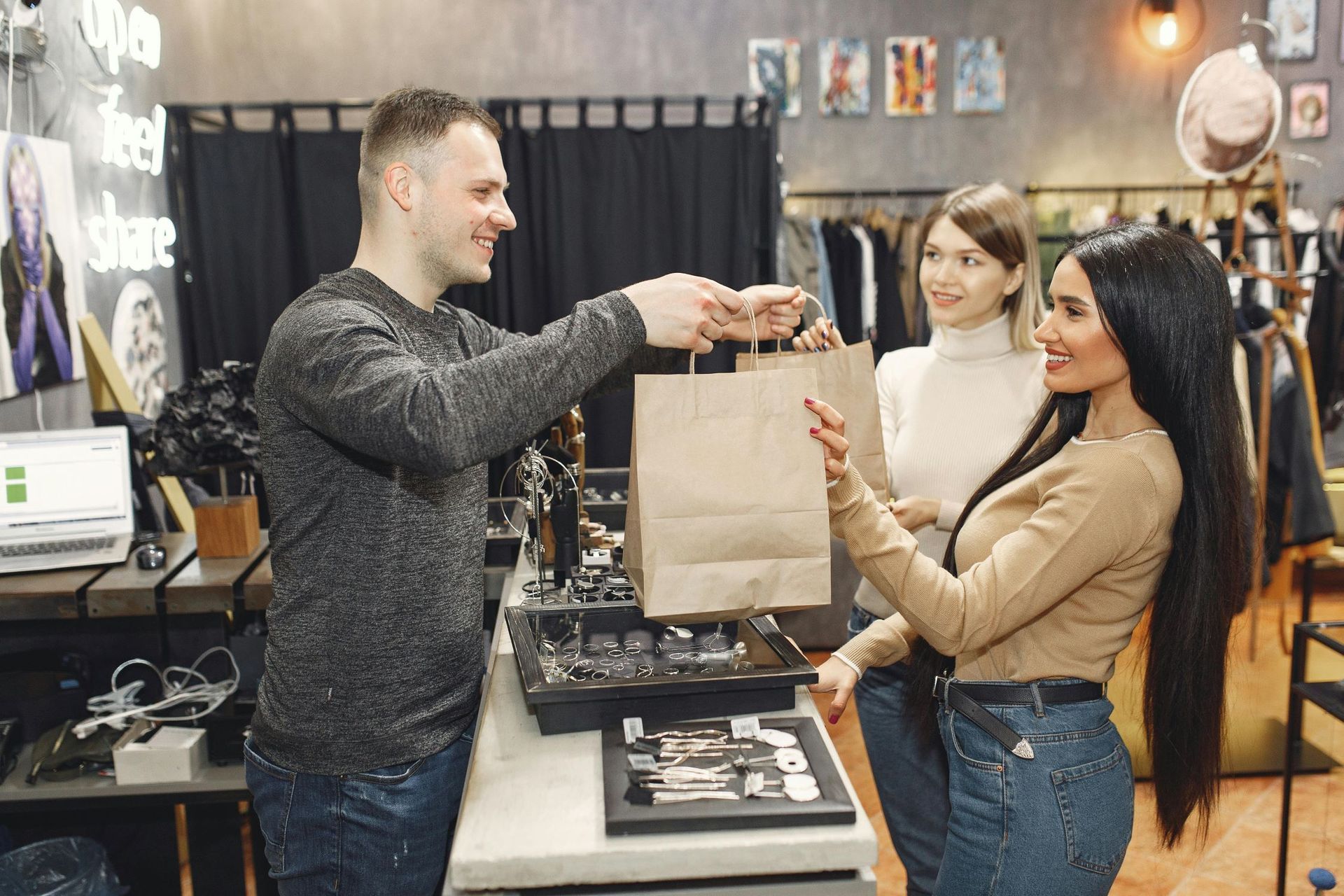 A male behind the counter is handing a paper bag to two ladies in front.