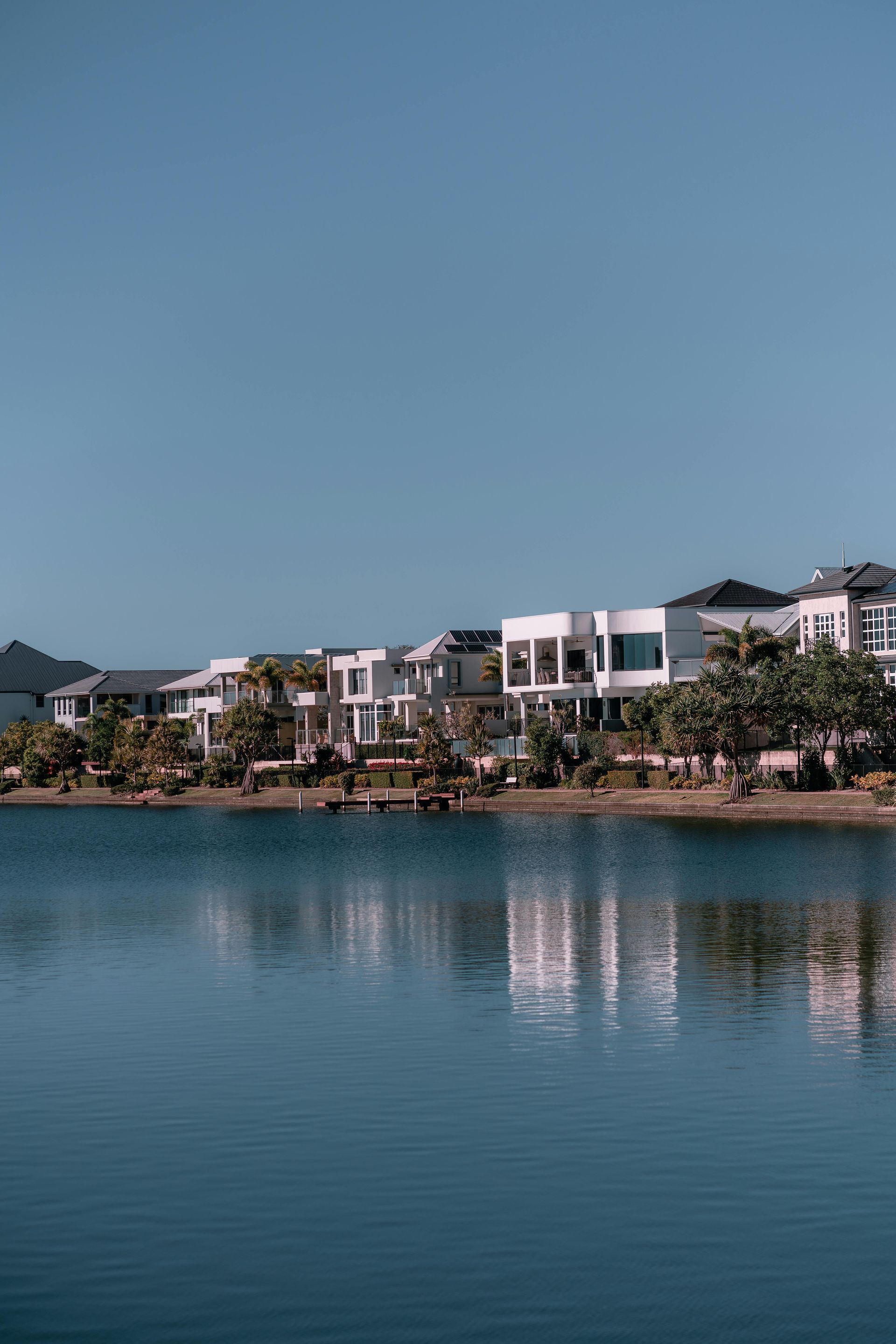 Modern waterfront apartments reflected in a calm blue lake under a clear sky