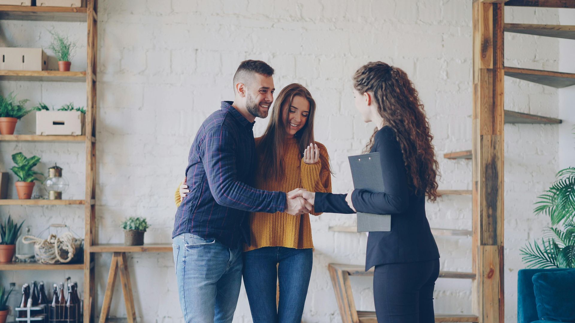 Three people discussing documents in a bright office with shelves and plants