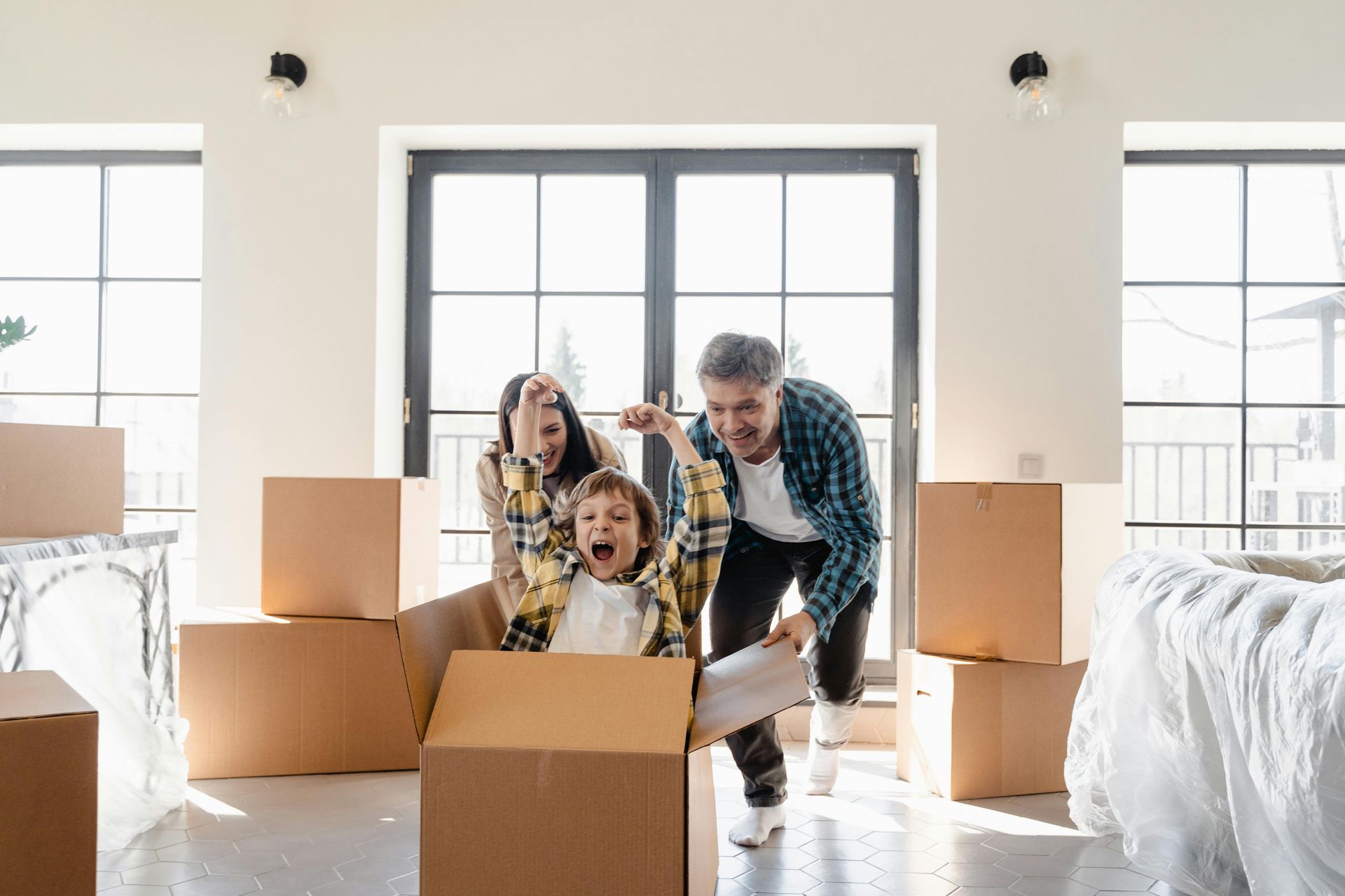 Family smiling among moving boxes in a bright, empty room
