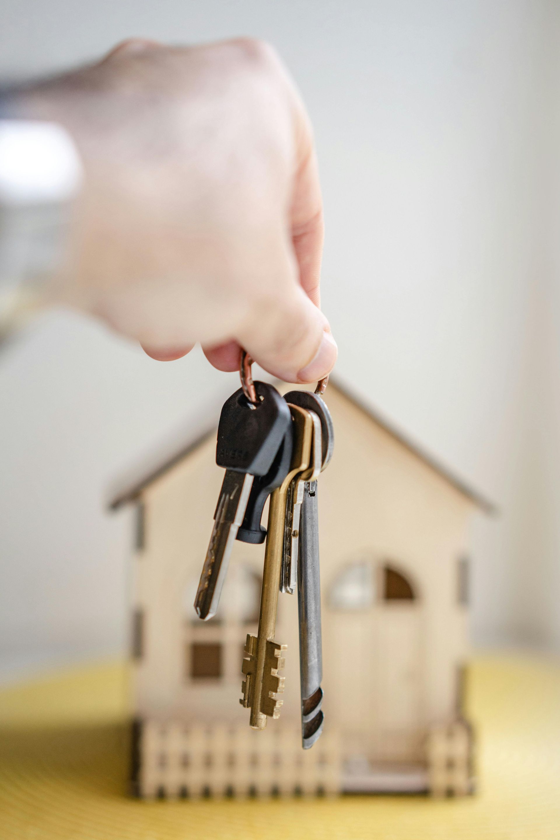 Hand holding a keyring in front of a small house model, suggesting home purchase or property access