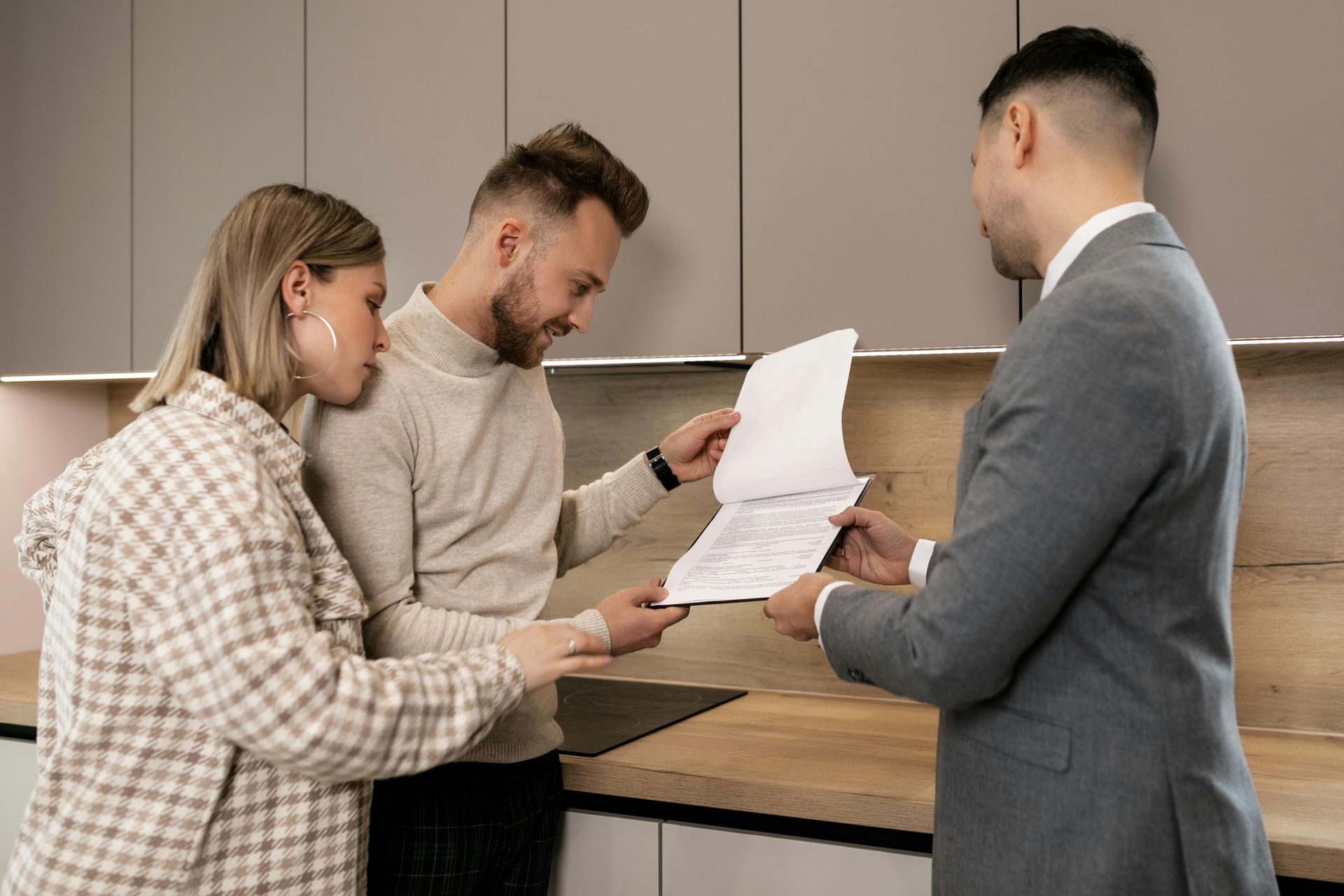 Two people review documents with a real estate agent in a modern kitchen.