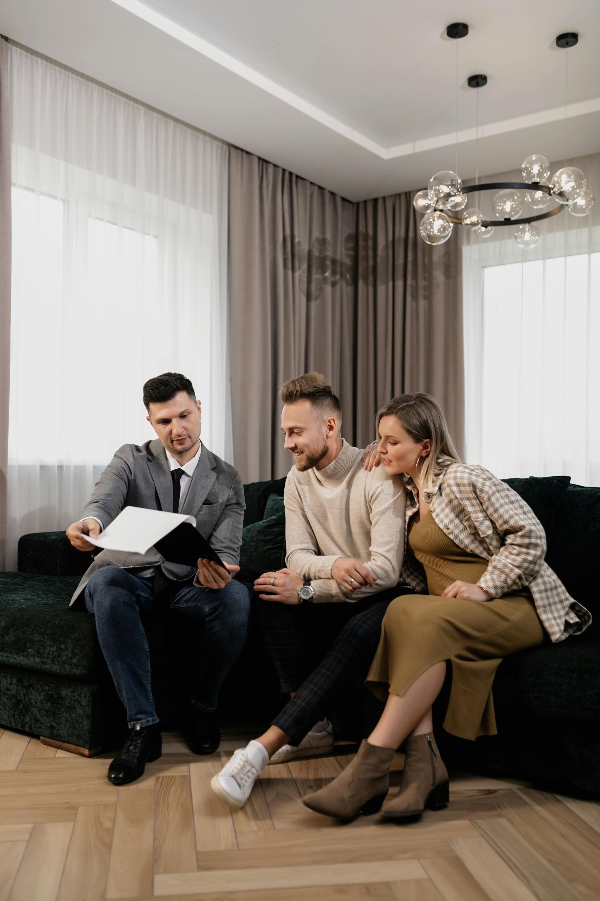 Three people sitting on a sofa, looking at a document in a bright modern living room.