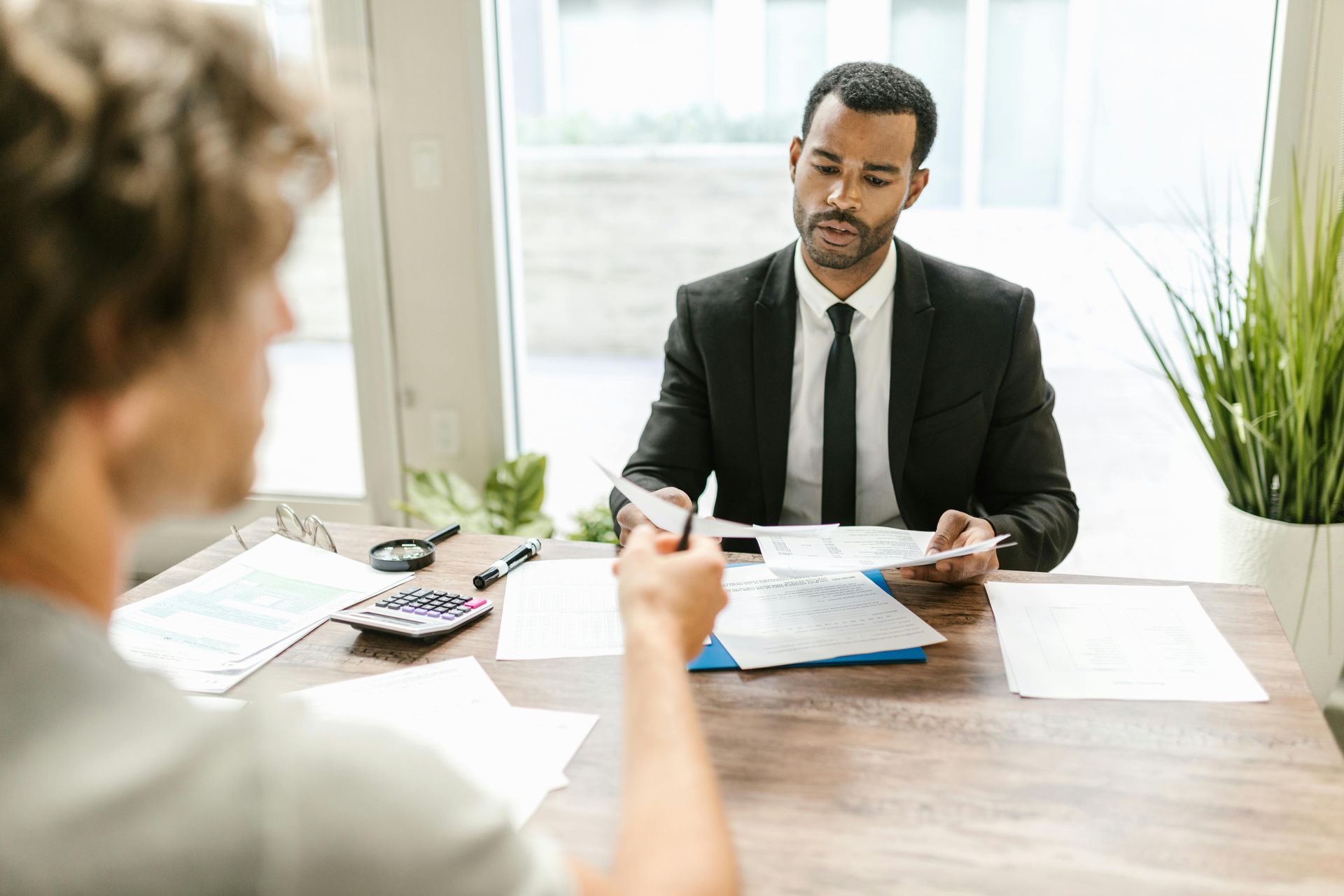 Job interview across a desk, with papers, pen, calculator, and a man in a suit reviewing documents.