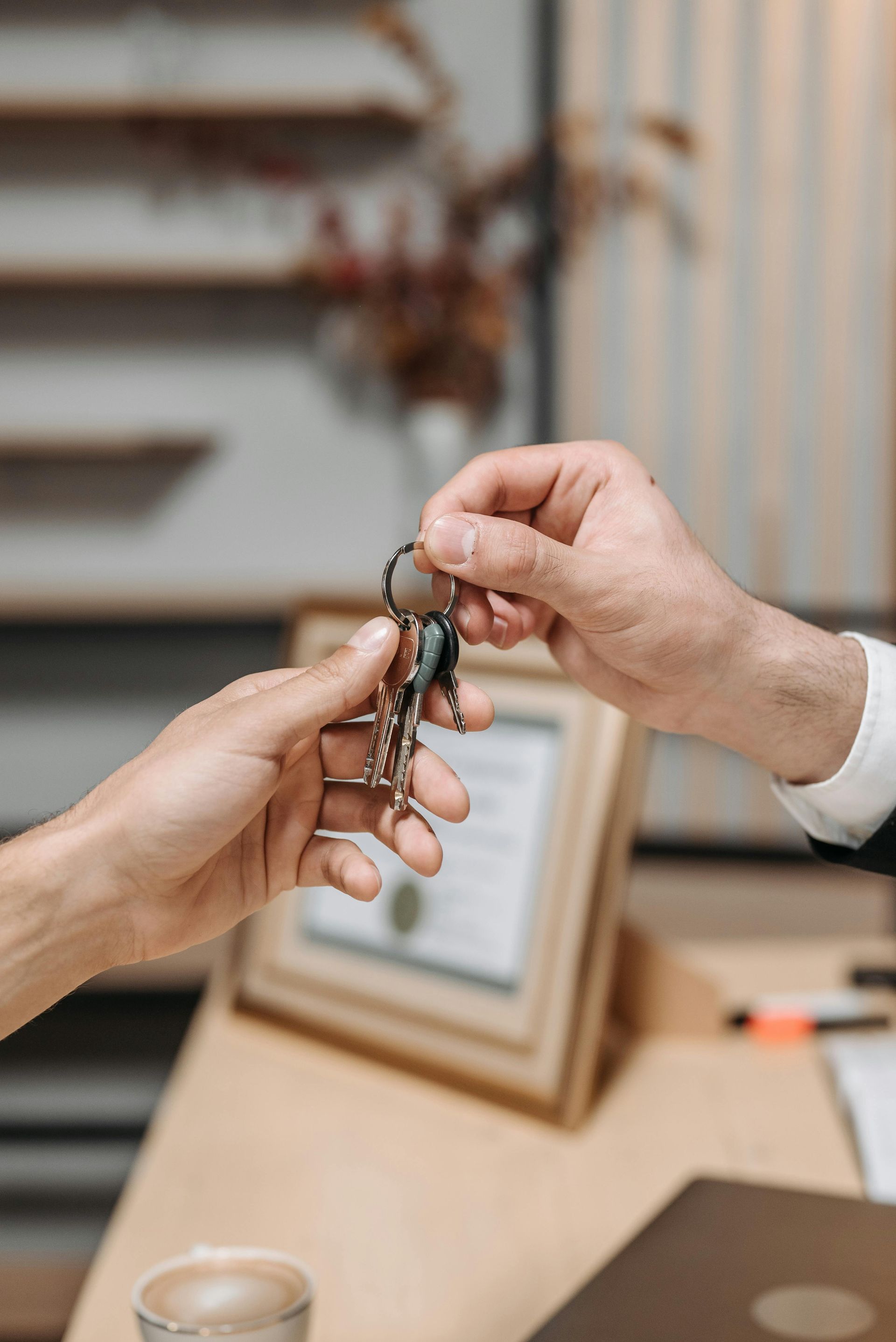 Hands exchanging keys over a desk in an office setting