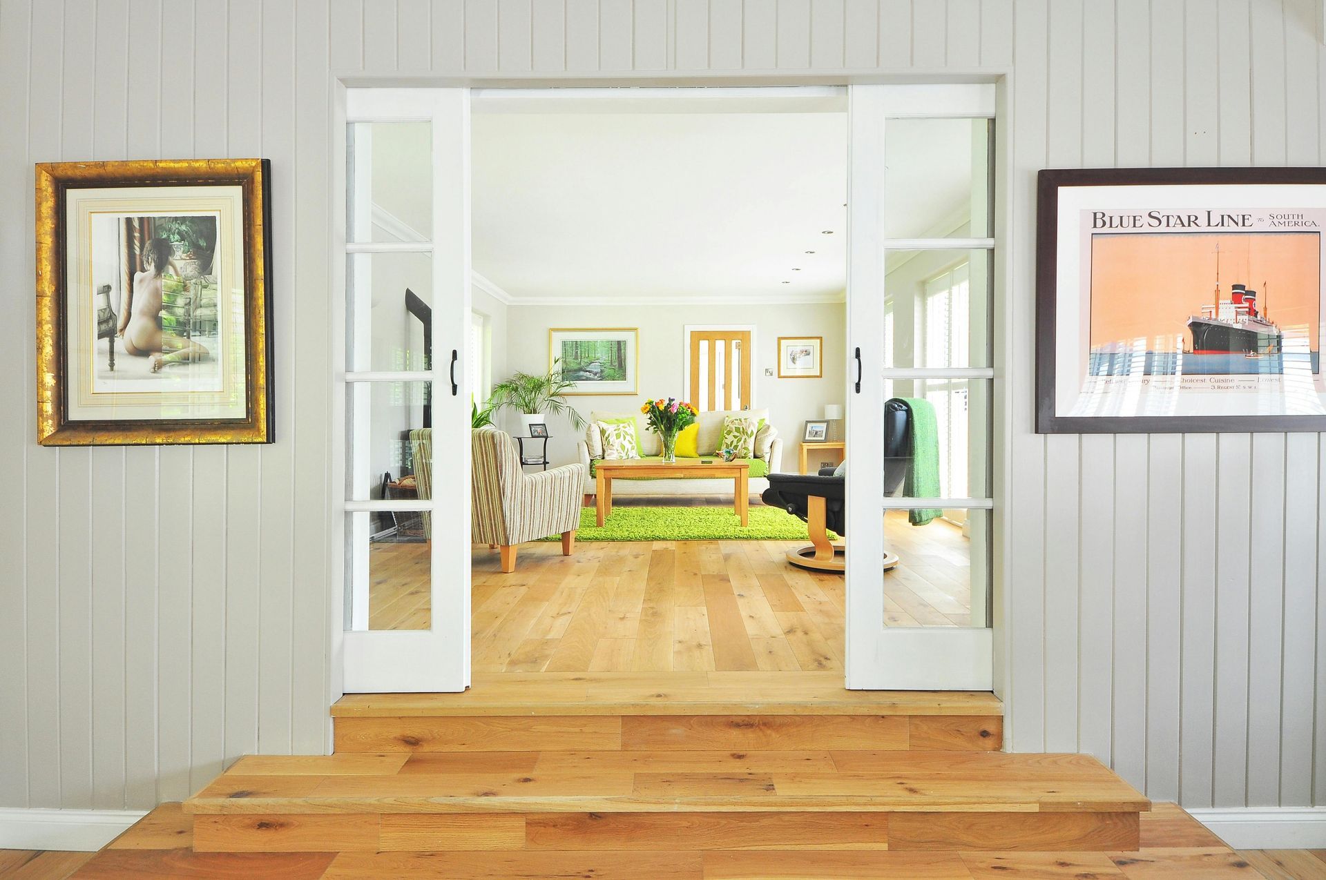 Bright living room with white French doors, wood floors, green sofa, and framed wall art