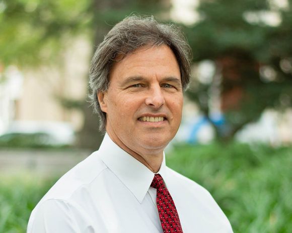 A man in a white shirt and red tie is smiling for the camera.