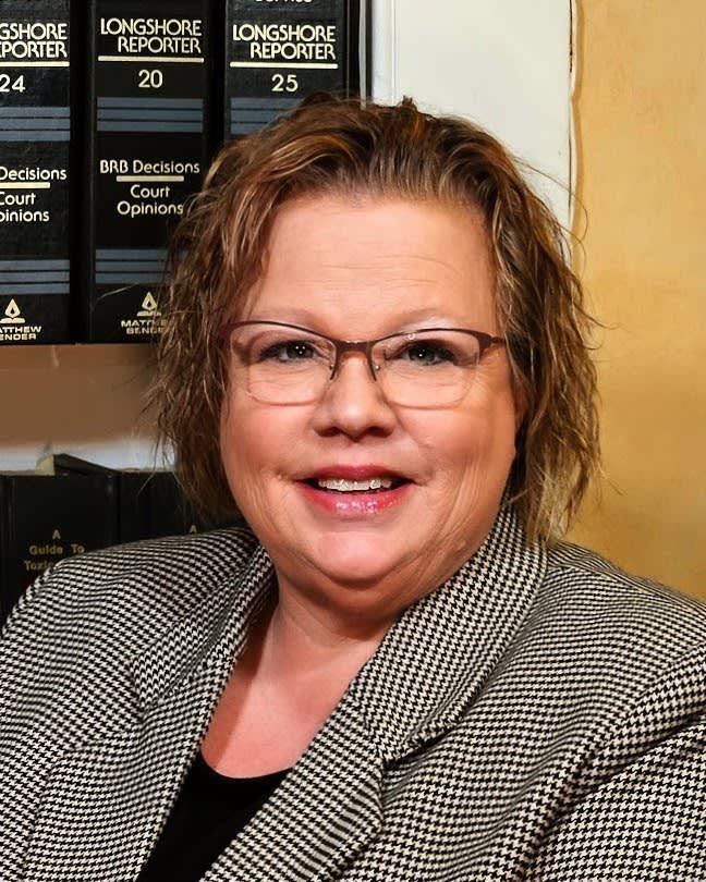 A woman wearing glasses is smiling in front of longshore reporter books