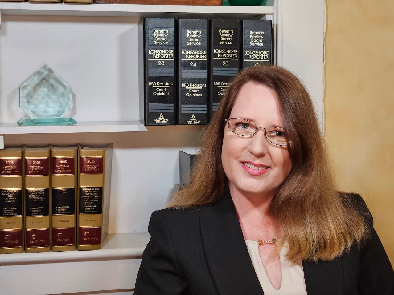 A woman wearing glasses is sitting in front of a bookshelf filled with books.