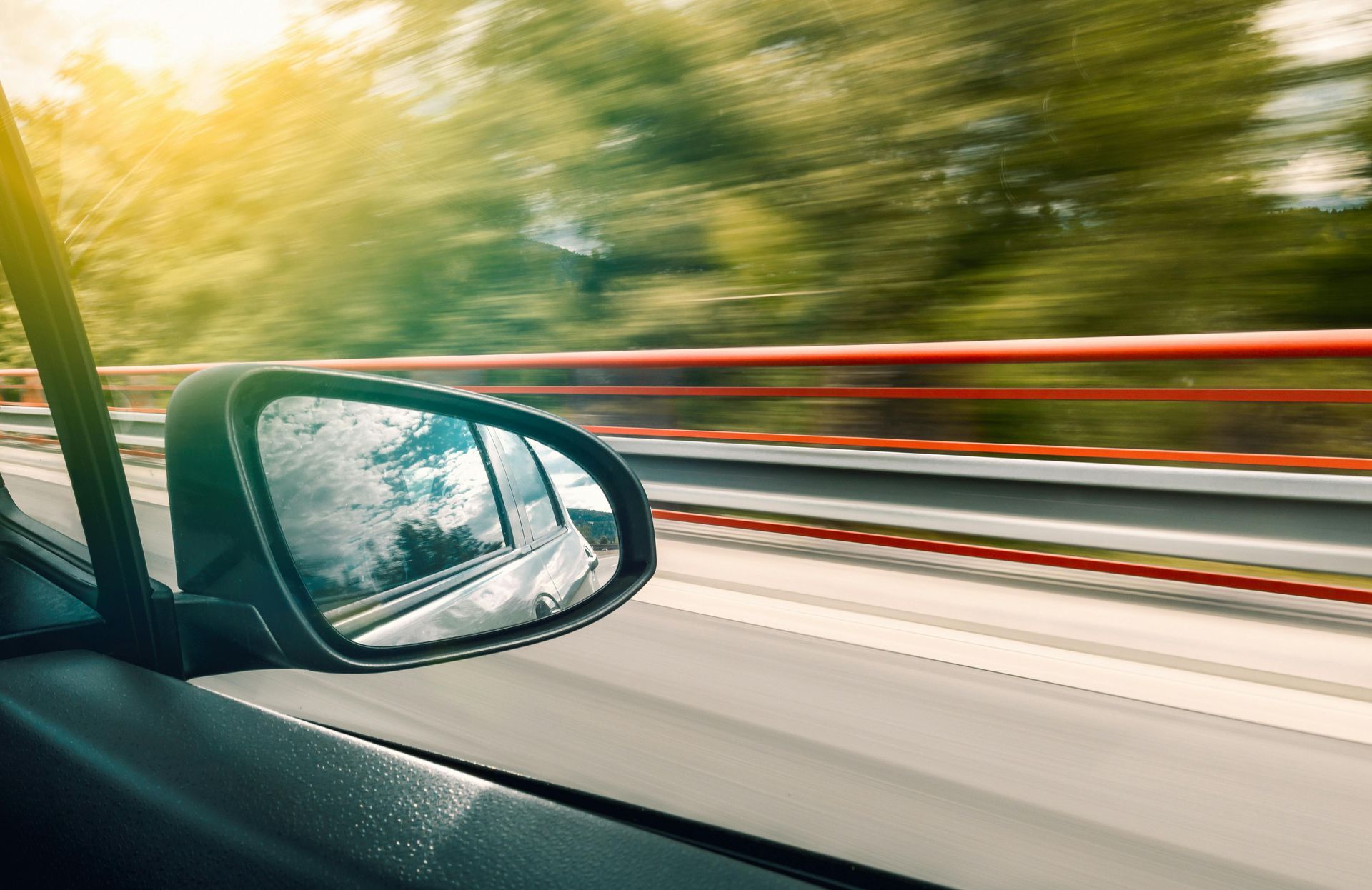 A car is driving down a highway and the rear view mirror is visible.