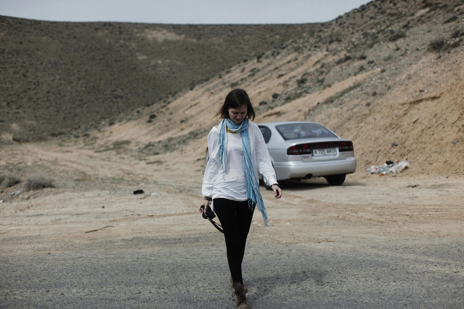 A woman walking down a dirt road with a car in the background