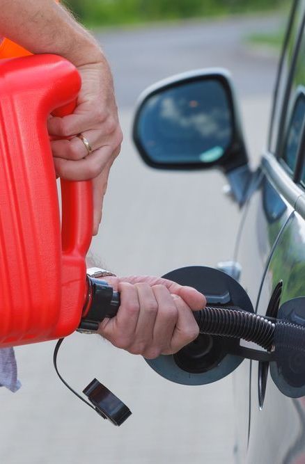 A person is pumping gas into a car with a red gas can