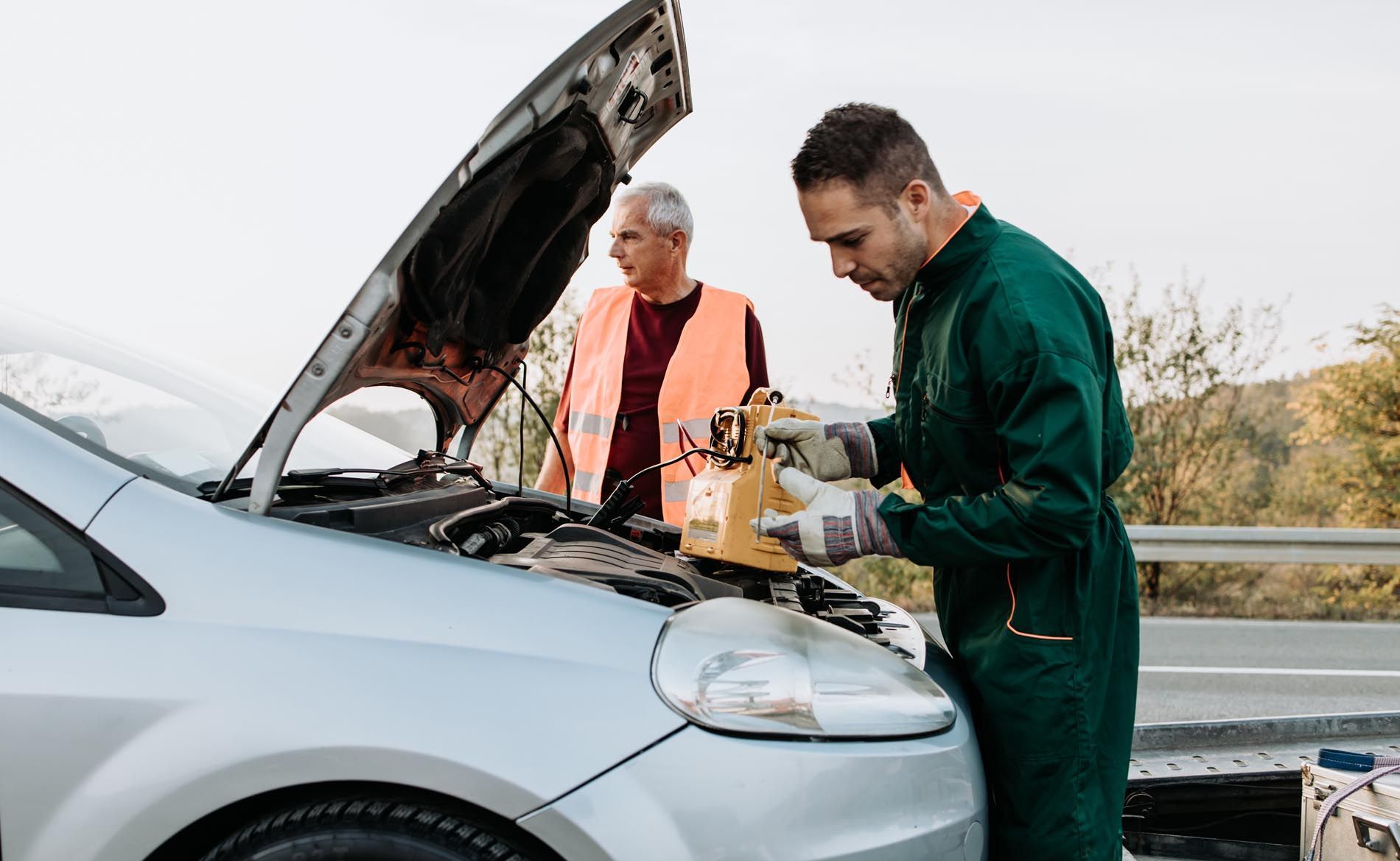 Two men are working on a broken down car on the side of the road.