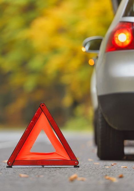 A red warning triangle is sitting on the side of the road next to a car.