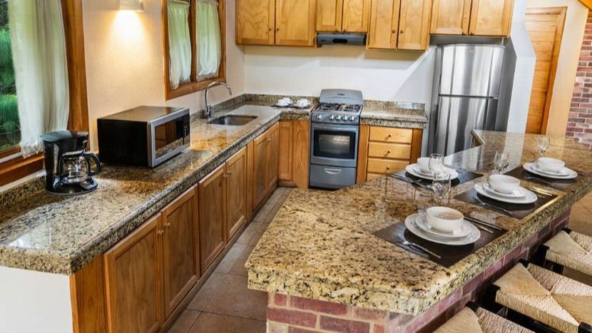 A kitchen with granite counter tops , stainless steel appliances , wooden cabinets and a brick island.