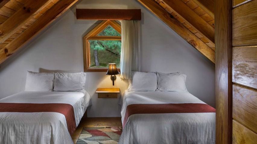 There are two beds in the attic of a cabin.