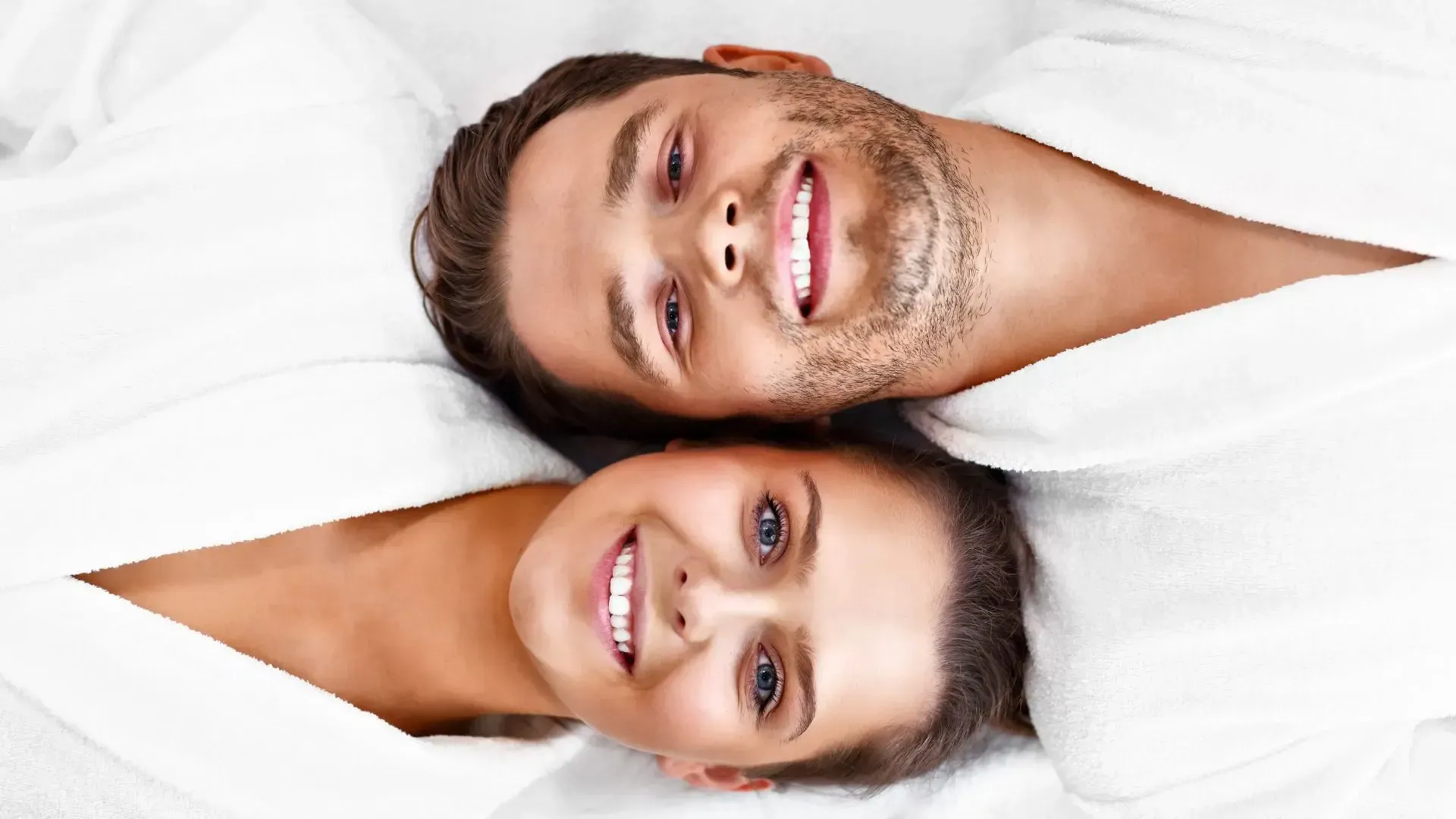 A man and a woman are laying next to each other on a bed and smiling.