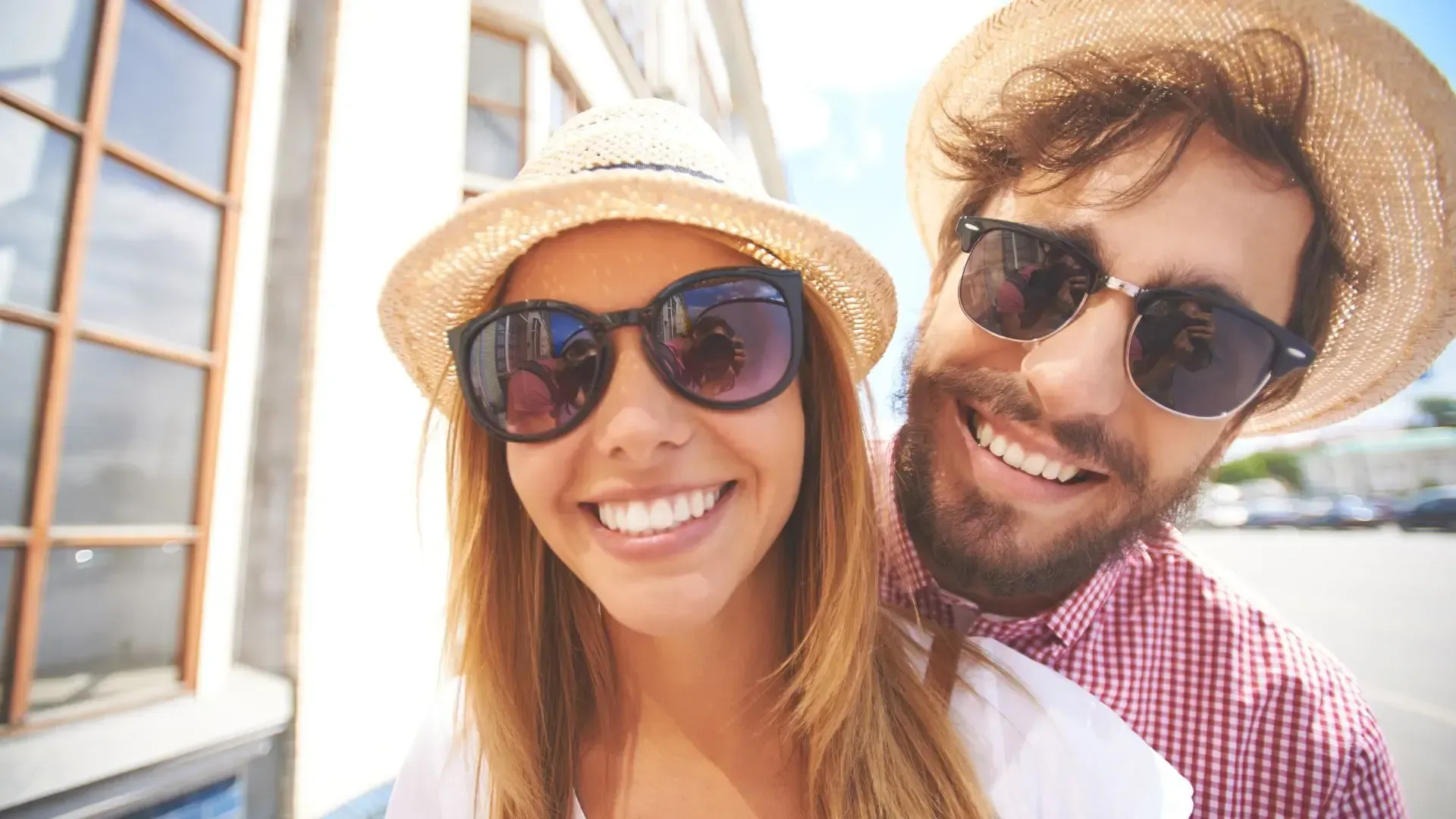 A man and a woman wearing hats and sunglasses are smiling for the camera.