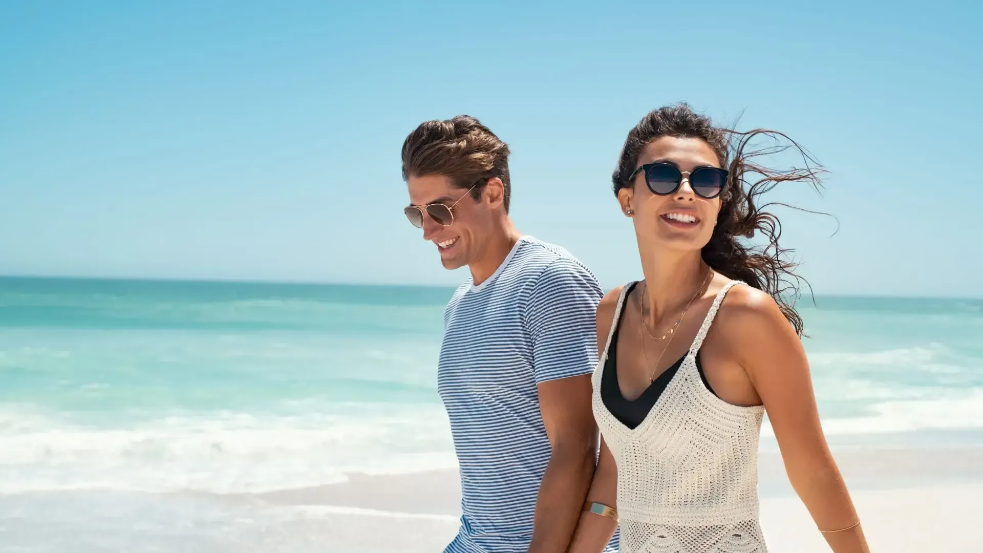 A man and a woman are walking on the beach holding hands.